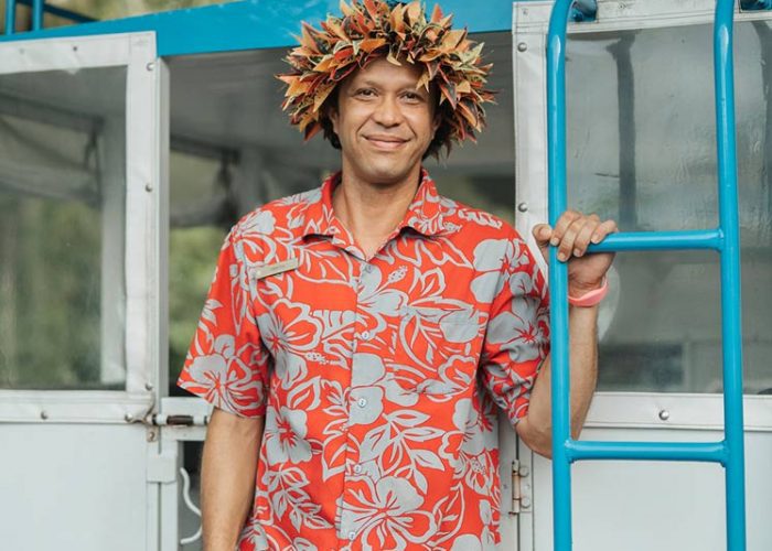 Warm Welcome in Traditional Polynesian Attire A man wearing traditional Polynesian attire and a flower crown, standing by a boat with a warm smile.